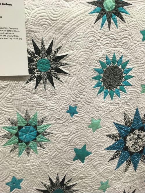 Small blue and gray Mariners Compass style stars on an intricately quilted white background.