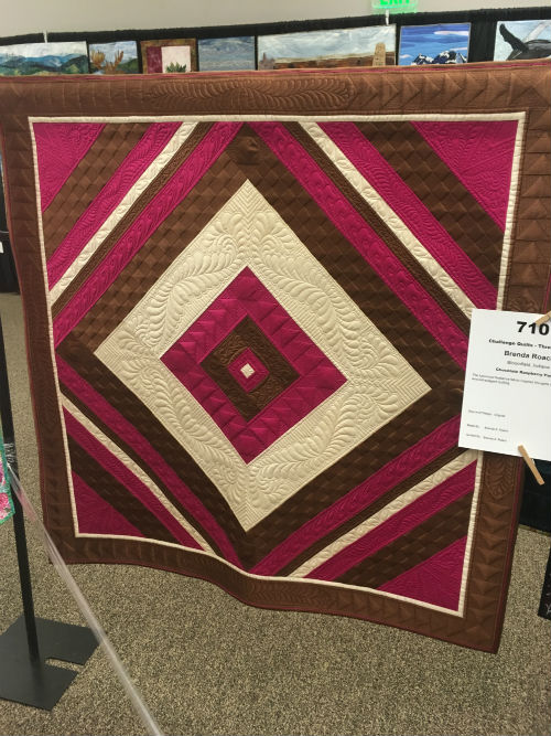 A three-color quilt in pink, brown, and cream, intricately quilted with interesting layering effects