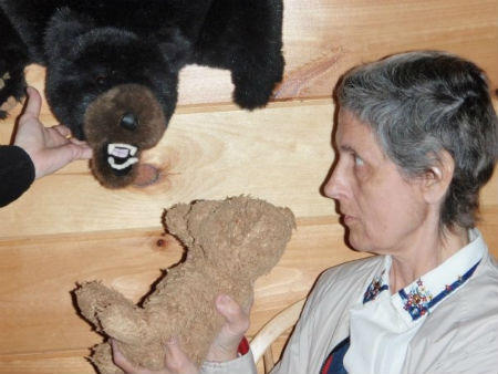 Mom holding up her sleeping teddy bear, Emerson, to meet a large fake bearskin rug bear head.