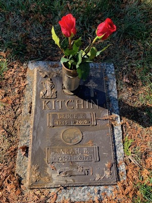 a photograph of my parents’ grave with two roses in a vase on it