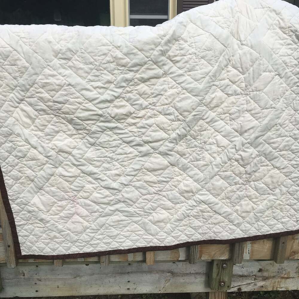 A full back view of the quilt. It has the same alternating star, border, and pinwheel pattern except it’s all a neutral muslin with small stitches. The border is quilted as cross-hatched diamonds.