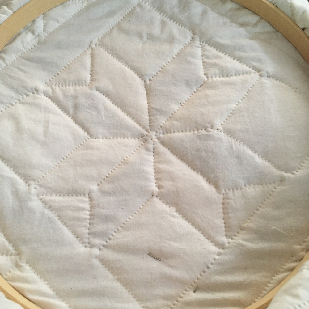 A view of the plain muslin backing while the quilt is still in its hoop. The stitching highlights the eight diamonds that make up the star.