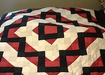 A quilt made in what resembles a log cabin diamond pattern with cream and red diamonds alternating out from the center. A jagged black line runs through them.