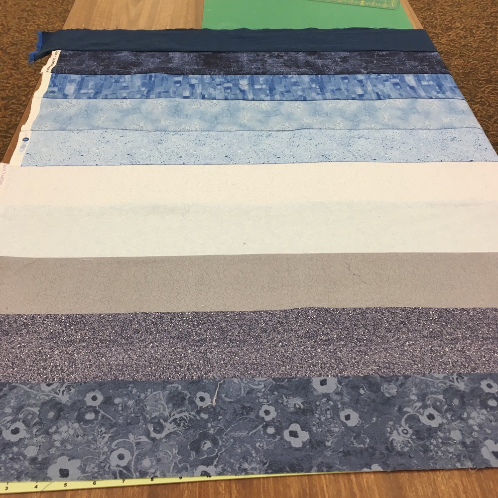 A giant square-ish block made of rows of dark gray/blue fabrics getting lighter into cream and light blue, then into patterend and darker blues
