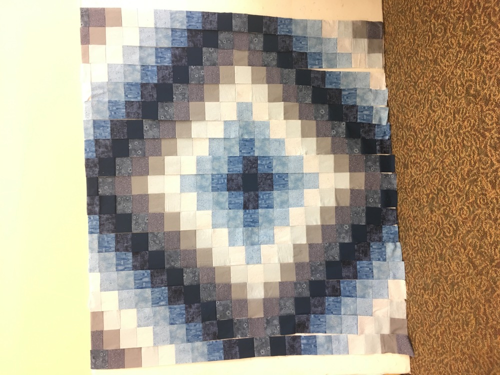 Offset quilt columns up on a design wall, taking the form of a diamond with colors radiating between deep blues, deep blue-grays, and cream/almost white light blue