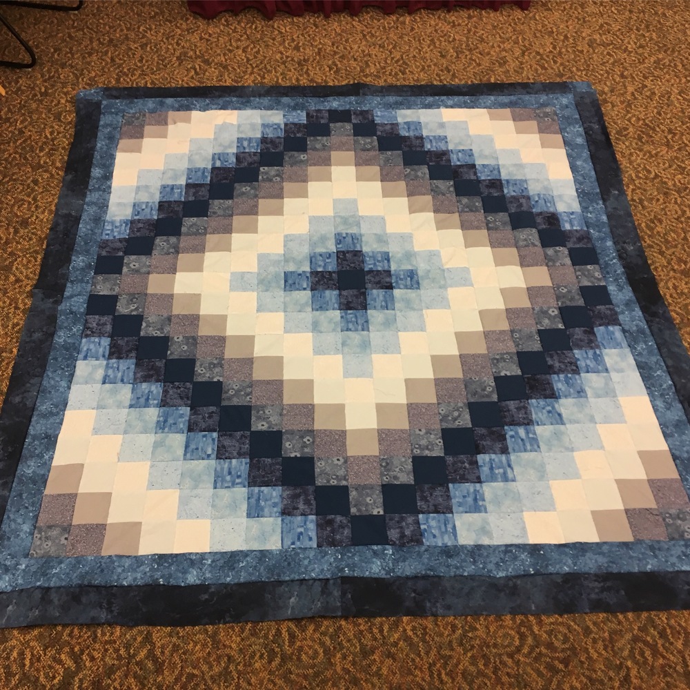 A quilt top lying on the floor with medium and dark bordders added around it. This makes the center colors pop a bit more.