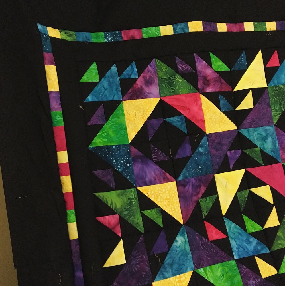 A closeup of the hanging unfinished quilt. You can make out some of the dark purples better than in the distant picture when they blend with the black.