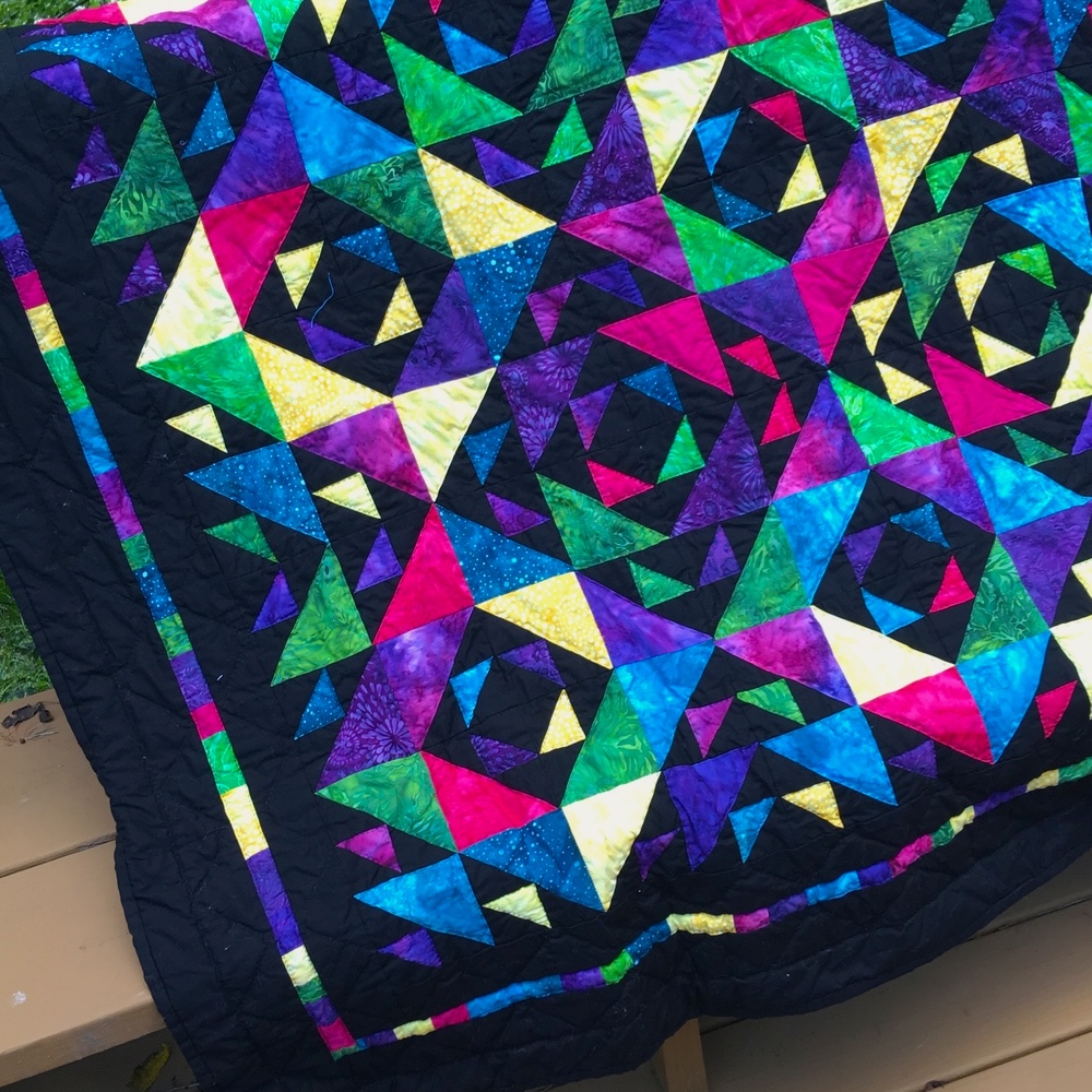 An outdoor closeup of the quilted top. Black quilting stitches are visible in batik squares.