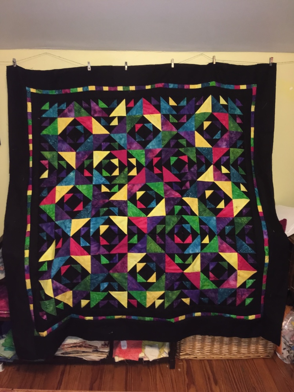 A pieced top hanging in my 2018 sewing room. It has diamonds in squares in diamonds with rich batiks alternating with black background. The indoor lighting makes some of the darker batiks contrast poorly with the black background but the yellow is quite rich.