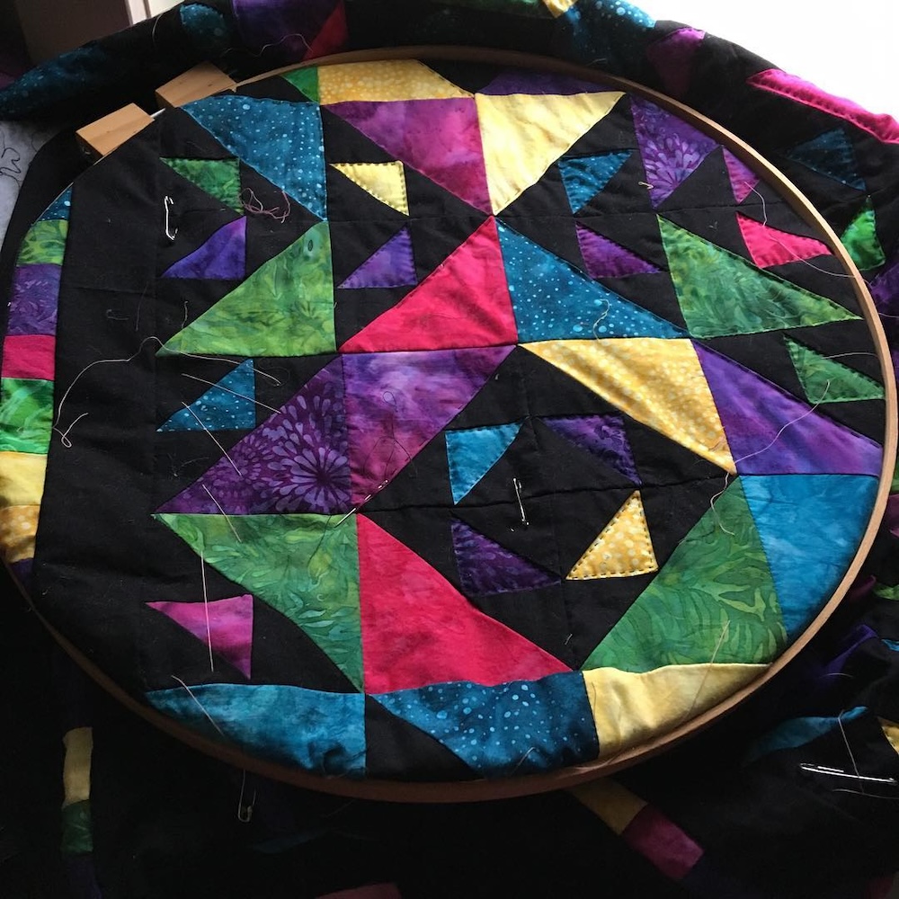 A segment of the quilt in a round lap hoop. The partial quilting is somewhat visible against bright batiks.