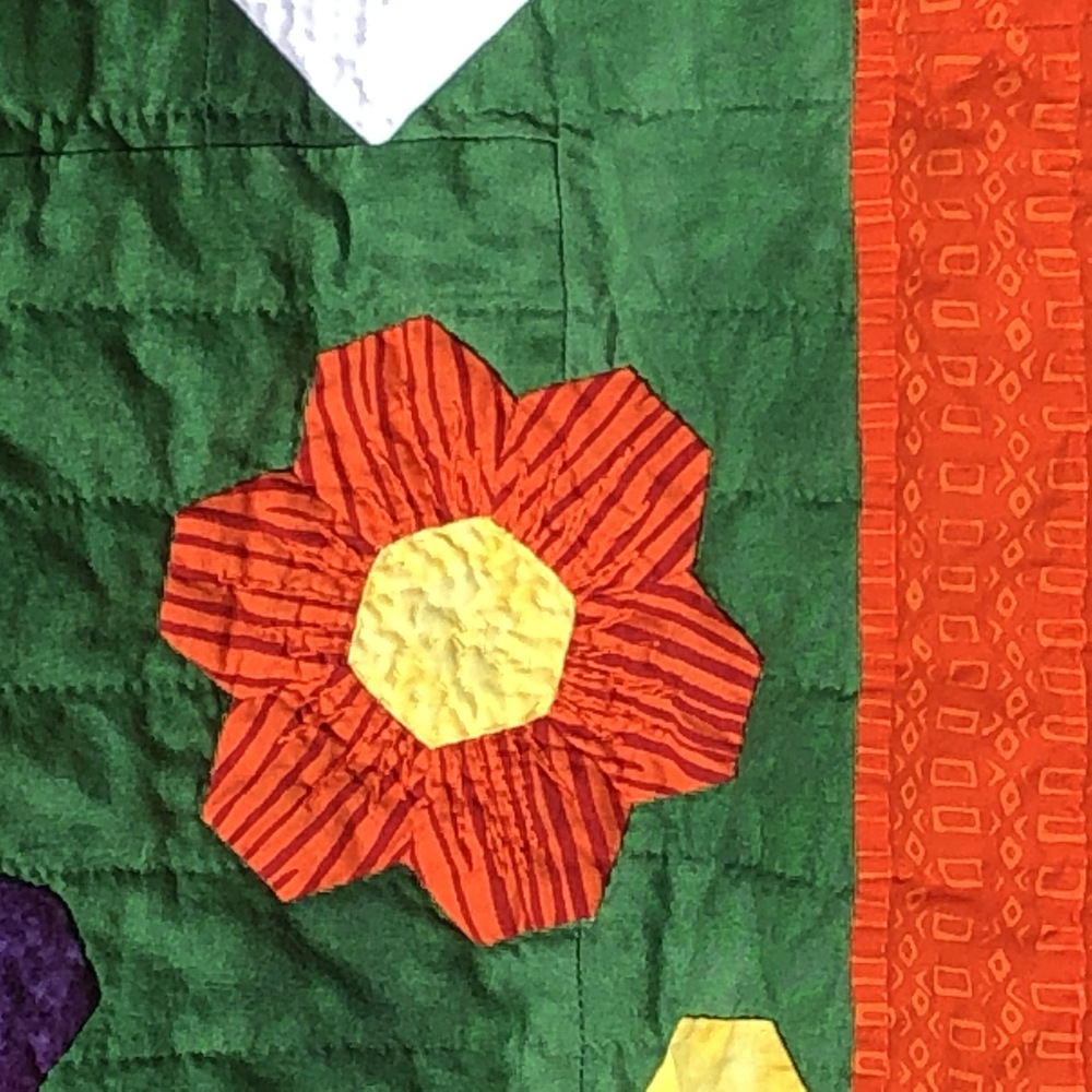 A closup of an orange flower made of hexagons. The fabric has stripes which all point outward like a real flower would