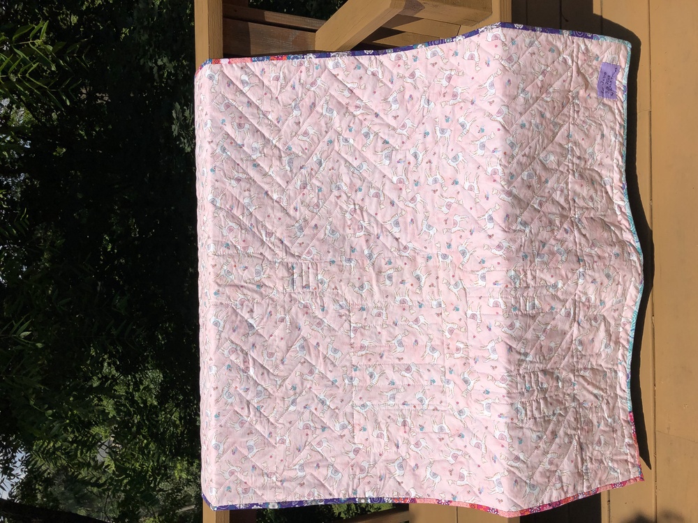 A picture of the full quilt from the back. It’s pink with various degrees of zig-zagging on it.