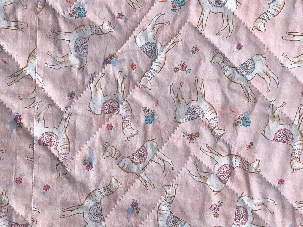 A closeup of the backing fabric. It’s pink with little llamas or alpacas wearing curved saddle blankets that somehwat resemble the large pieced llama