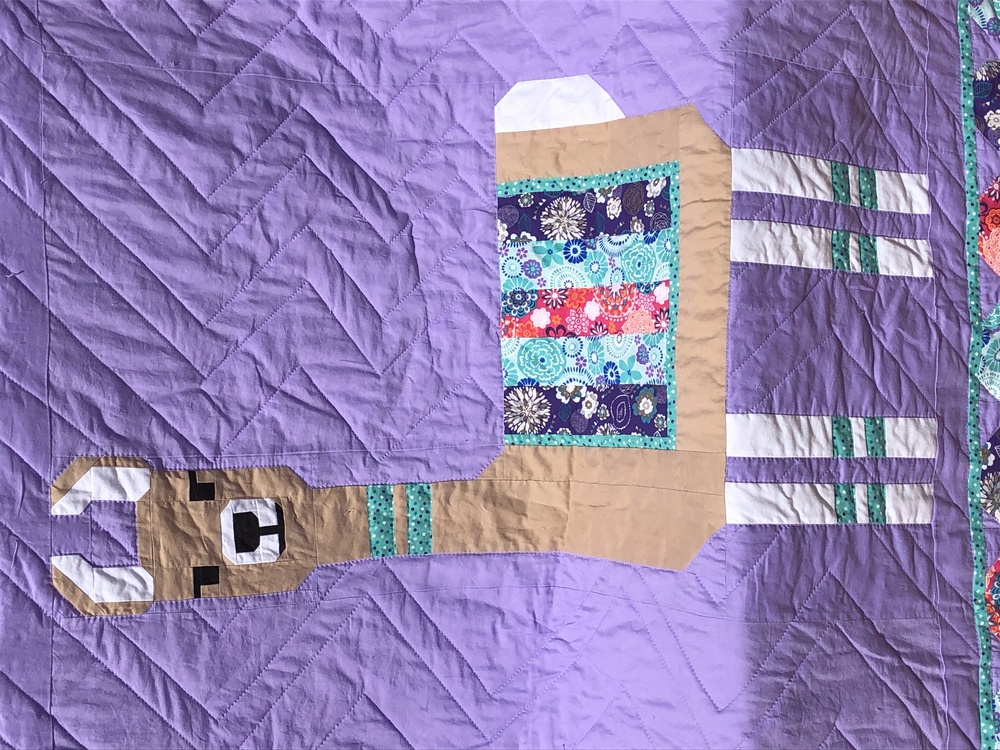 A closeup of the llama pattern and the front of the quilt. You can really see a zig-zag hand-sitthced pattern behind it on the background.
