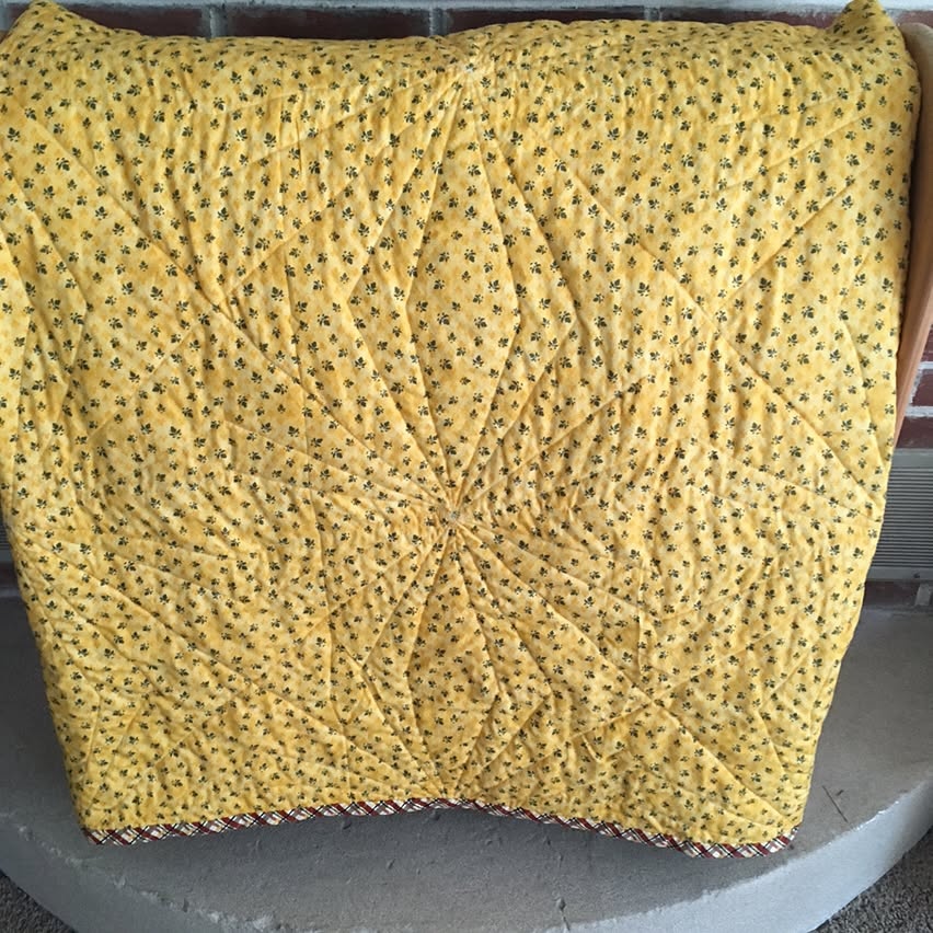 A yellow backing with small flowers on it. The star or flower-like quilted pattern is very obvious