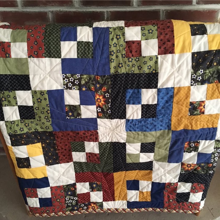 A quilt made up of nearly log-cabin like blocks with rich medium-tone and dark-tone fabrics. Diagonal runs of small and medium white blocks separate them. The colorful bits make a kind of augmented plus sign between the diagonal rows. It's got quilting lines that form 90-degree diamonds with might more angular nested diamonds inside them.