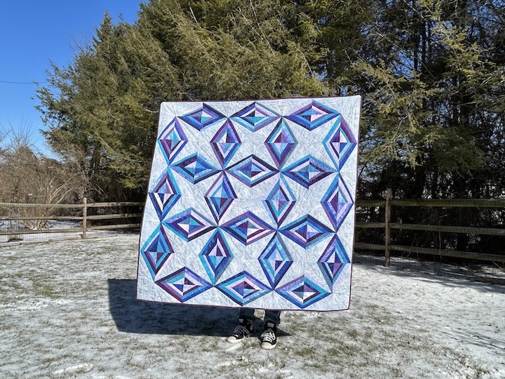 a quilt composed of strip-pieced diamonds in blue and purple on a gray background